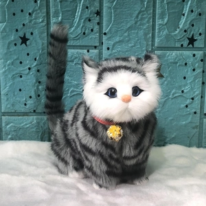 Realistic grey tabby plush cat toy with a blue collar and bell standing on a white rug