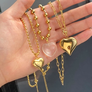 Detailed view of hand holding three gold heart pendant necklaces with beaded and O-chains
