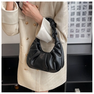 Detail of black pleated shoulder bag with knotted handle held by model in tweed jacket