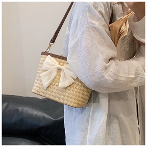 Detail of woven straw bucket bag with large white chiffon bow and brown leather strap