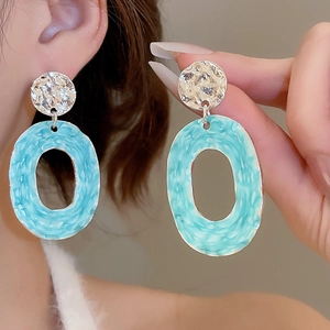 Macro view of light blue enamel oval pendant earrings with silver pleated texture details