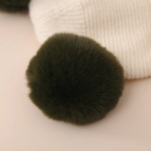 Close-up of soft fluffy green faux fur pom-pom on creamy white knitted winter hat fabric