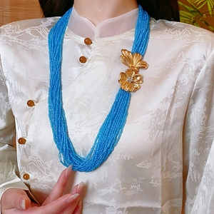 Detail of layered blue beaded necklace with golden butterfly and flower charm accents