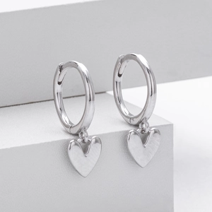 Close-up of polished S925 sterling silver heart dangle earrings on a white stand