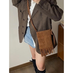 Close-up of brown suede crossbody bag with long tassels on a female model in casual style