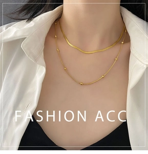 Detail of layered gold snake chain necklace with beads on woman wearing white shirt