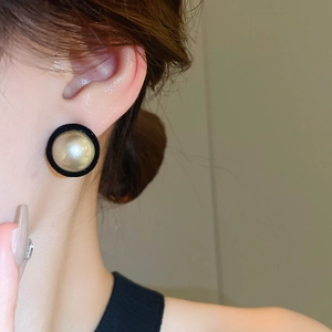 Close-up of minimalist velvet pearl stud earrings worn by a model in black and gold