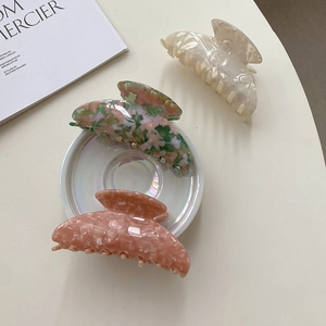 Trois grandes pinces à cheveux en acétate crème, rose et marbré sur un plateau blanc