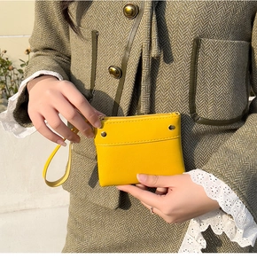 Detail of yellow leather mini pouch with metal zipper and wrist strap on green coat