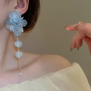 Detail shot of light blue acrylic flower earrings with long gold tassel on a model