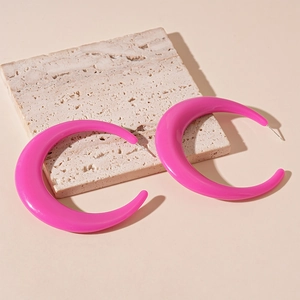 Macro view of oversized magenta acrylic C-shaped earrings on a textured stone base