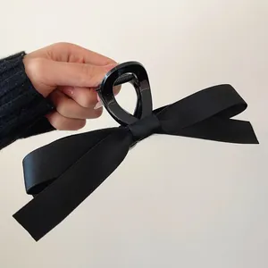 Detail of a large black satin bow hair claw clip with a glossy shark clip mechanism