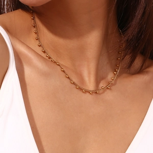 Close-up of 18K gold plated beaded chain necklace on a model wearing a white V-neck