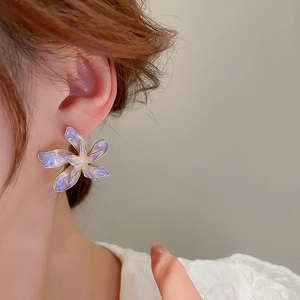 Gros plan d'une boucle d'oreille fleur dégradé violet avec bordure dorée portée à l'oreille
