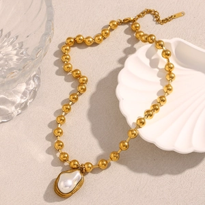 Golden bead chain necklace with baroque pearl pendant on a beige textured background