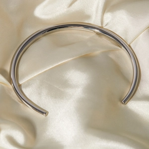 Close-up of polished silver stainless steel rigid collar necklace on silk fabric