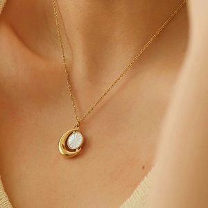 Elegant gold moon necklace with white shell inlay worn on a delicate sweater chain