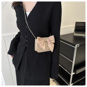 Small beige crossbody bag for women with large elegant bow and sleek metal chain strap.