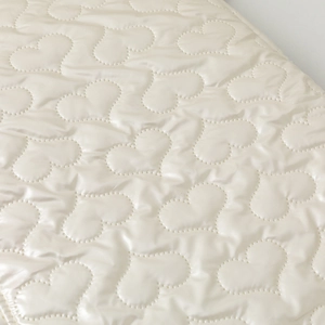 Close-up of heart-shaped quilted padding on a soft cream laptop bag with a silky finish