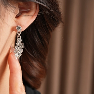Macro shot of silver diamond-encrusted geometric tassel earrings on a model