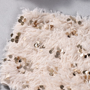 Dettaglio macro del tessuto peluche albicocca con paillettes dorate e consistenza morbida