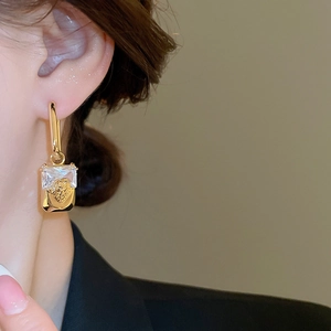 Close-up of gold geometric lion head earrings with inset rectangular crystals on model