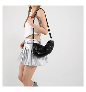 Detail of the knotted shoulder strap and glossy crinkled leather on a black crescent bag
