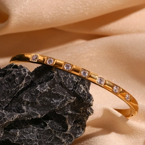 Detailed macro view of 18K gold plated bangle with inlaid zircons on black rock background