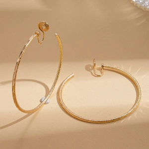 Detail eines mattierten 18k vergoldeten Clip-Ohrrings auf warmem beigefarbenem Hintergrund