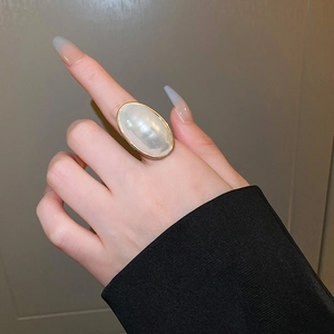 Gros plan d'une bague dorée ornée d'une grande pierre ovale blanc nacré au doigt