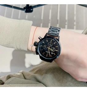 Detailed shot of a black stainless steel quartz watch with gold dial markers on a wrist