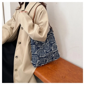Detail of blue denim tote bag featuring white floral patterns and raw fringe edges