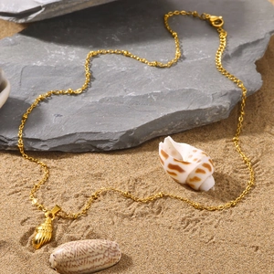 Golden seashell charm necklace on sand with starfish and rocks in beach setting
