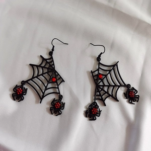 Macro detail of black spider web earrings with red rhinestones and fringe tassels
