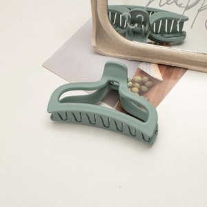 Macro detail of a large matte green shark hair claw clip on an artistic mirror background