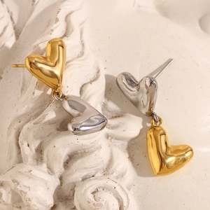 Close-up of dual-tone 18K gold and silver plated heart stud earrings on a plaster base