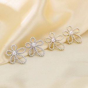 Detailed view of pearl flower stud earrings in gold and silver on yellow silk fabric