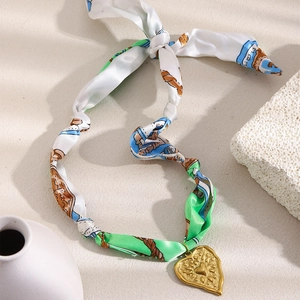 18K gold-plated heart pendant on green silk scarf necklace against a beige background