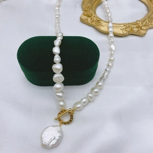 Macro shot of baroque pearl necklace with golden OT clasp on white silk backdrop