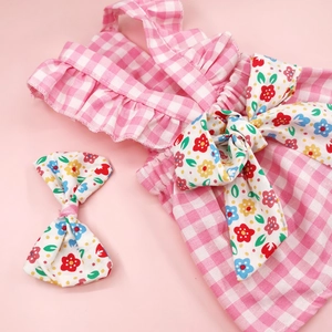 Detail of pink plaid dog dress with colorful floral bow and matching hair accessory