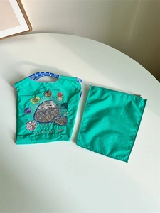 Close-up of green nylon organizer with detailed embroidery and matching zipper pouch