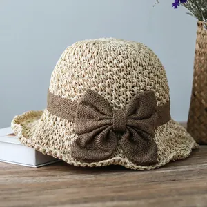 Detail of breathable straw sun hat featuring a large brown fabric bow on the brim