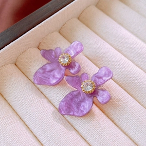 Macro shot of purple flower stud earrings with shimmering resin petals and crystal centers