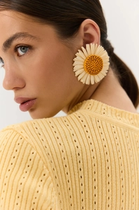 Dettaglio di orecchini a fiore all'uncinetto con centro giallo e petali bianchi su modella