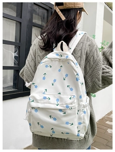 Detail shot of a white floral backpack featuring blue tulip patterns worn by a model