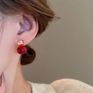 Close-up of translucent double sphere earrings in amber and deep red resin on ear