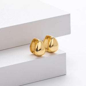Close-up of golden teardrop hoop earrings with polished mirror finish on white steps