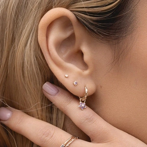 Detail of gold earrings set with purple zircon studs and a small star charm hoop earring