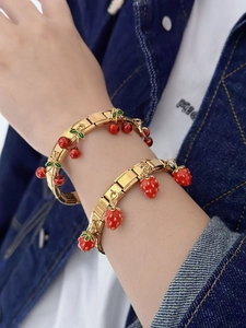 Close-up of golden elastic bracelets with red strawberry and cherry charms on a wrist