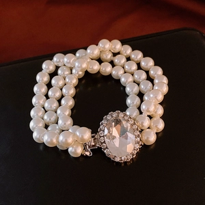 Détail d'un bracelet de perles à trois rangs avec un grand strass ovale sur cuir noir